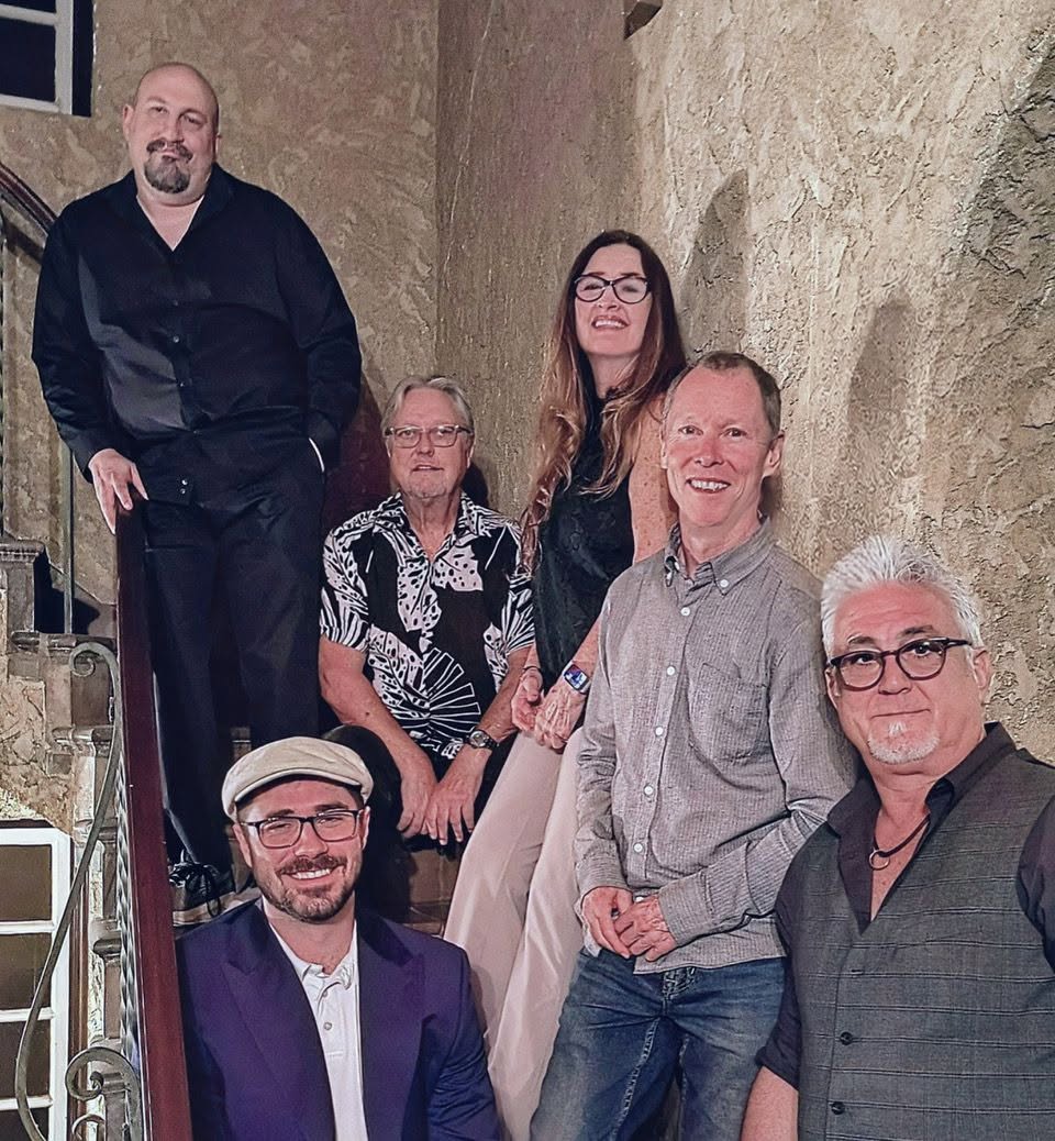 The St Pete Collective band, seven musicians posed on a stucco stairway